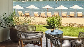 Une terrasse dotée de chaises et d’une table en osier, offrant une vue sur une plage parsemée de parasols et de chaises longues.
