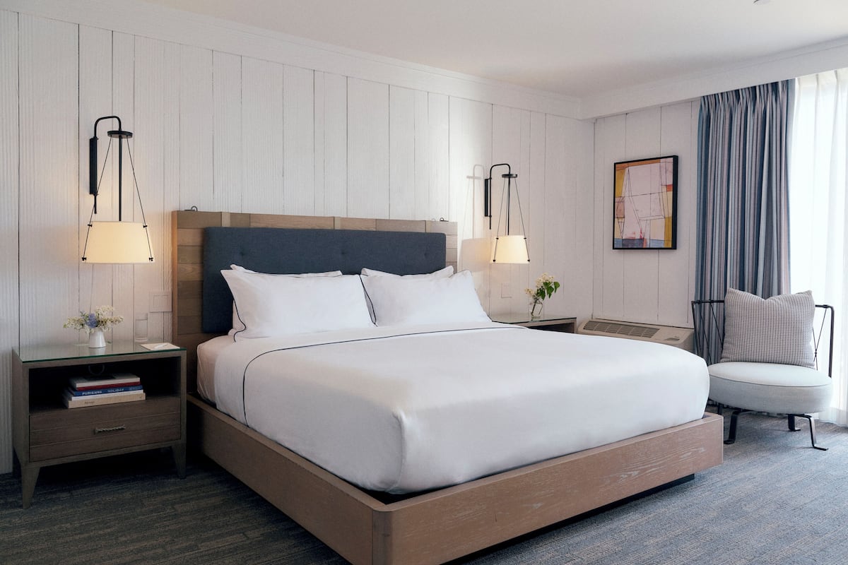 A modern hotel room with a large bed, two bedside tables, a chair, and a window with curtains.