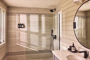 Une salle de bain moderne dotée d’une douche à parois de verre, d’un grand miroir et d’un meuble-lavabo.