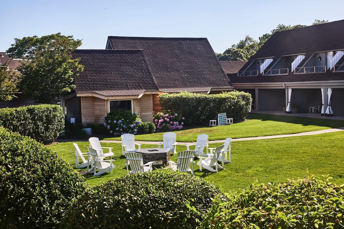A house with a sloped roof, a lawn with white chairs, and a small table.