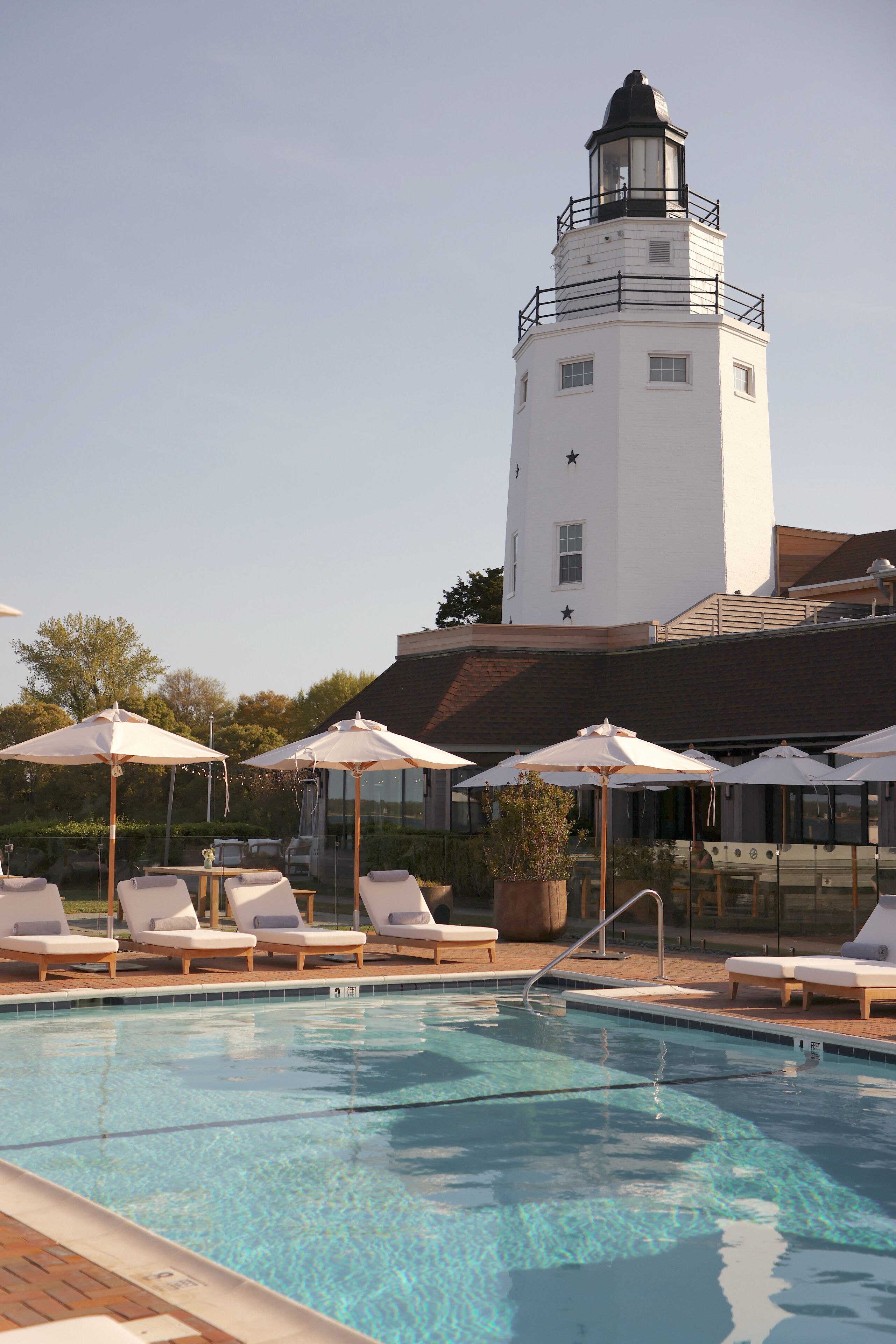 A swimming pool with lounge chairs and umbrellas, a white building with a tower, and a clear sky.