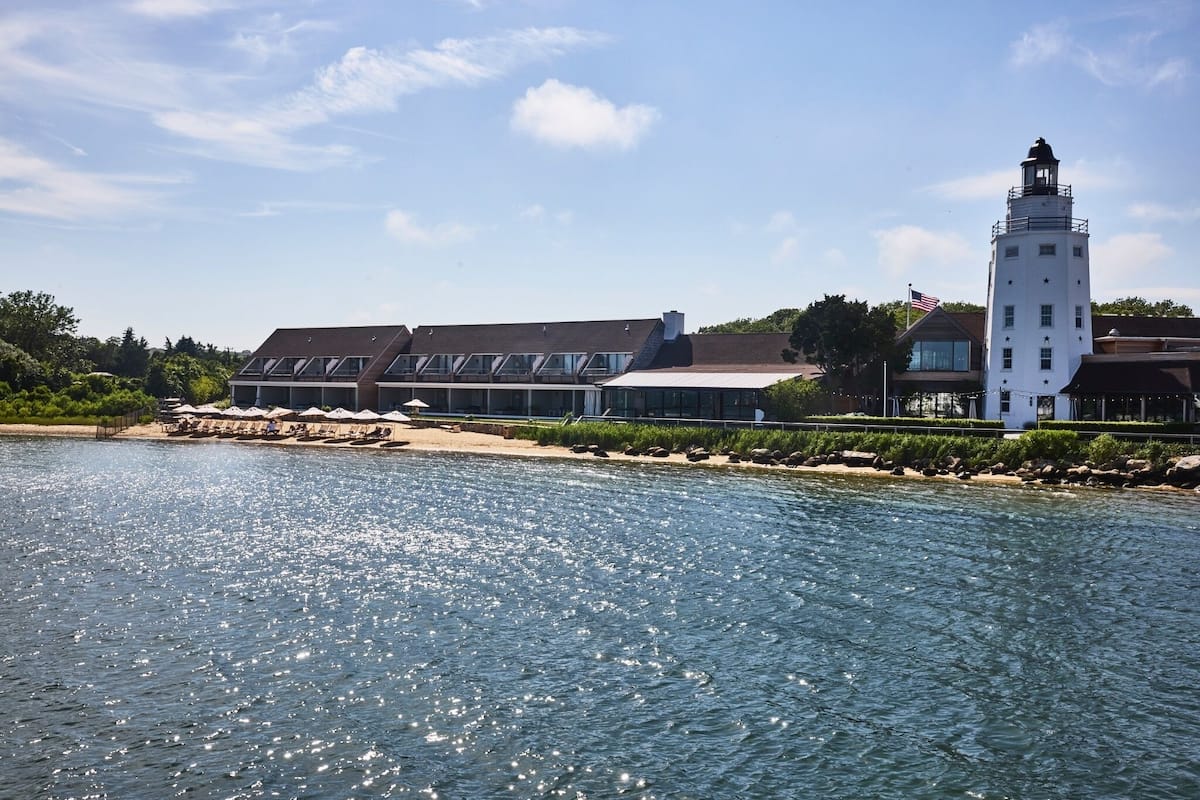 A waterfront hotel with a prominent lighthouse, a beach area with umbrellas, and a clear view of the water.