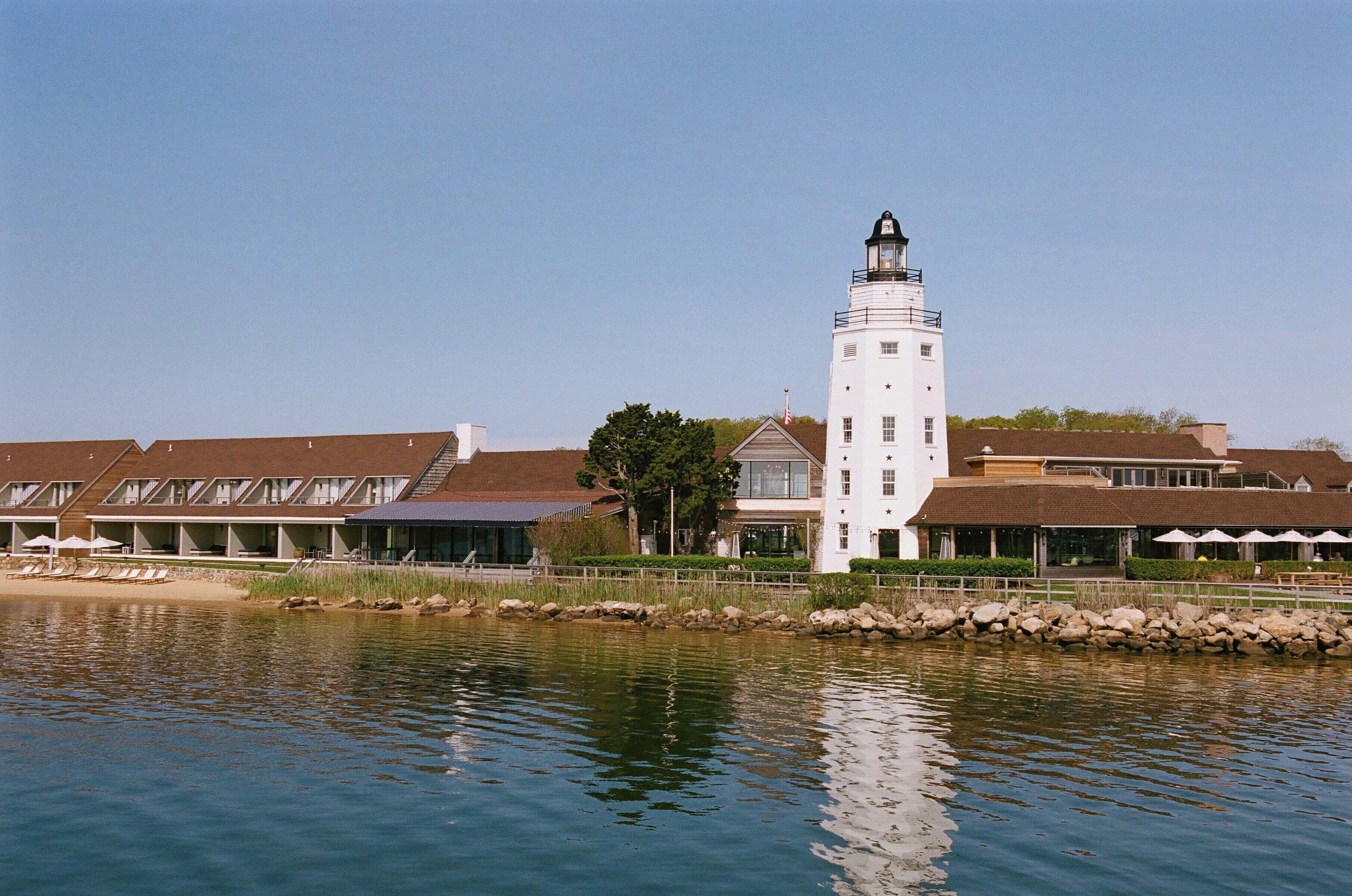 A white lighthouse with a black top, surrounded by a building with multiple windows and a balcony.