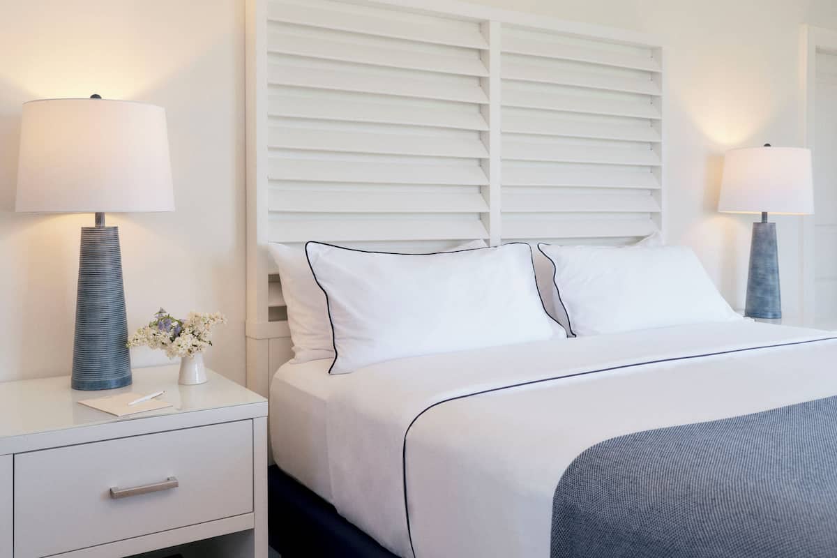 A neatly arranged hotel room with a bed, bedside tables, lamps, and a small vase with flowers.