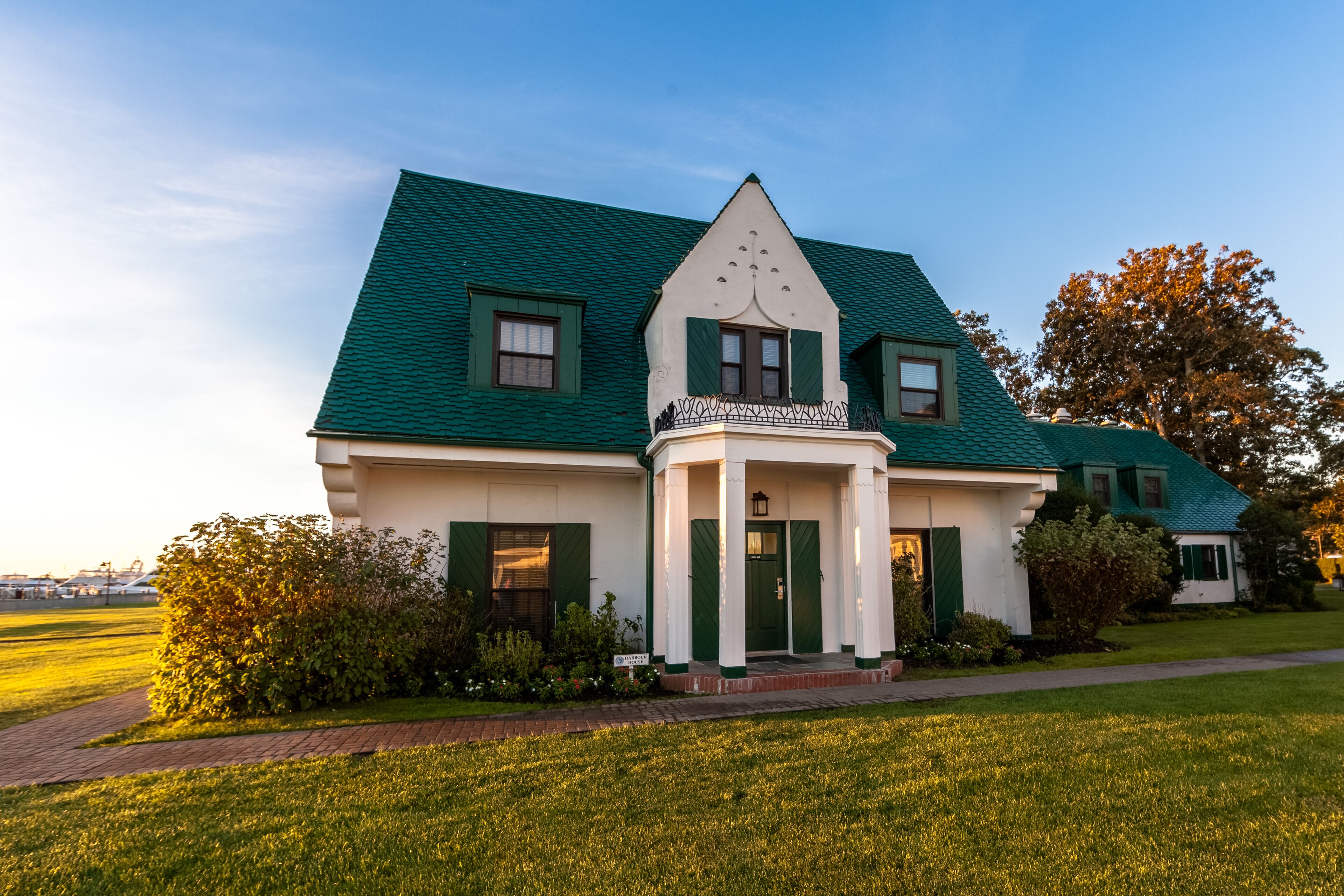 A large, two-story house with a green roof and white walls, featuring a prominent front porch and a well-maintained lawn.