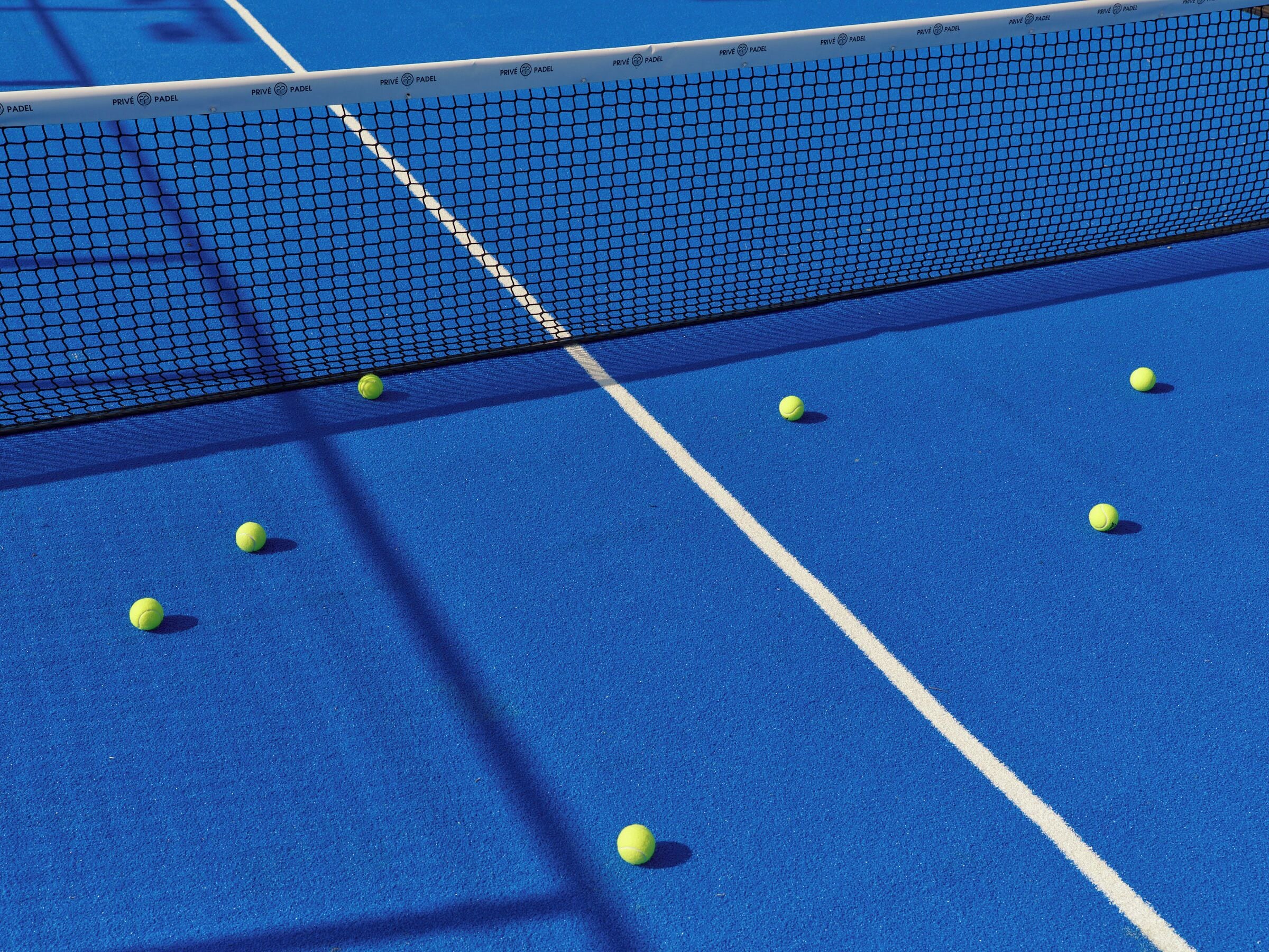 Ein blauer Tennisplatz mit Netz und mehreren Tennisbällen.