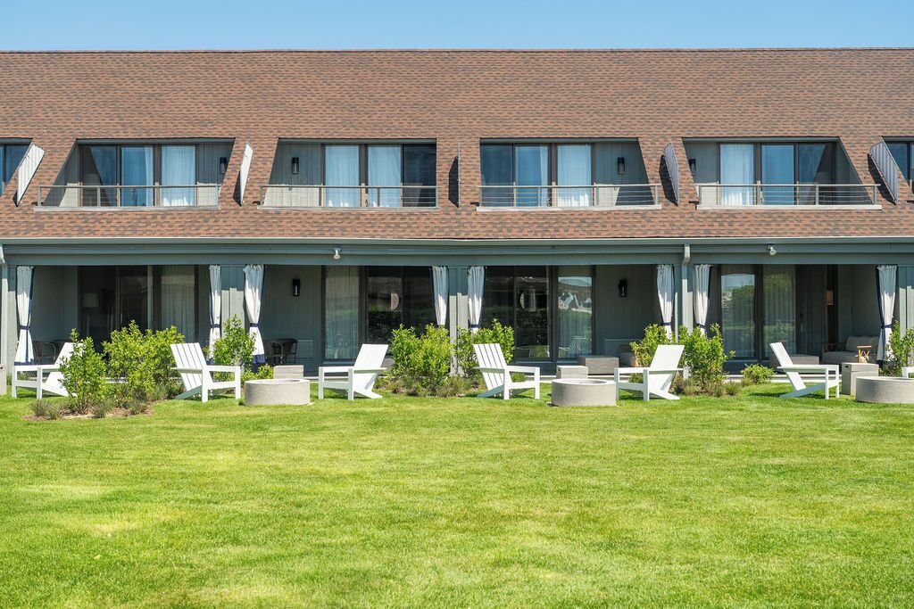 A building with a flat roof, multiple windows, and a covered outdoor seating area with chairs and planters.