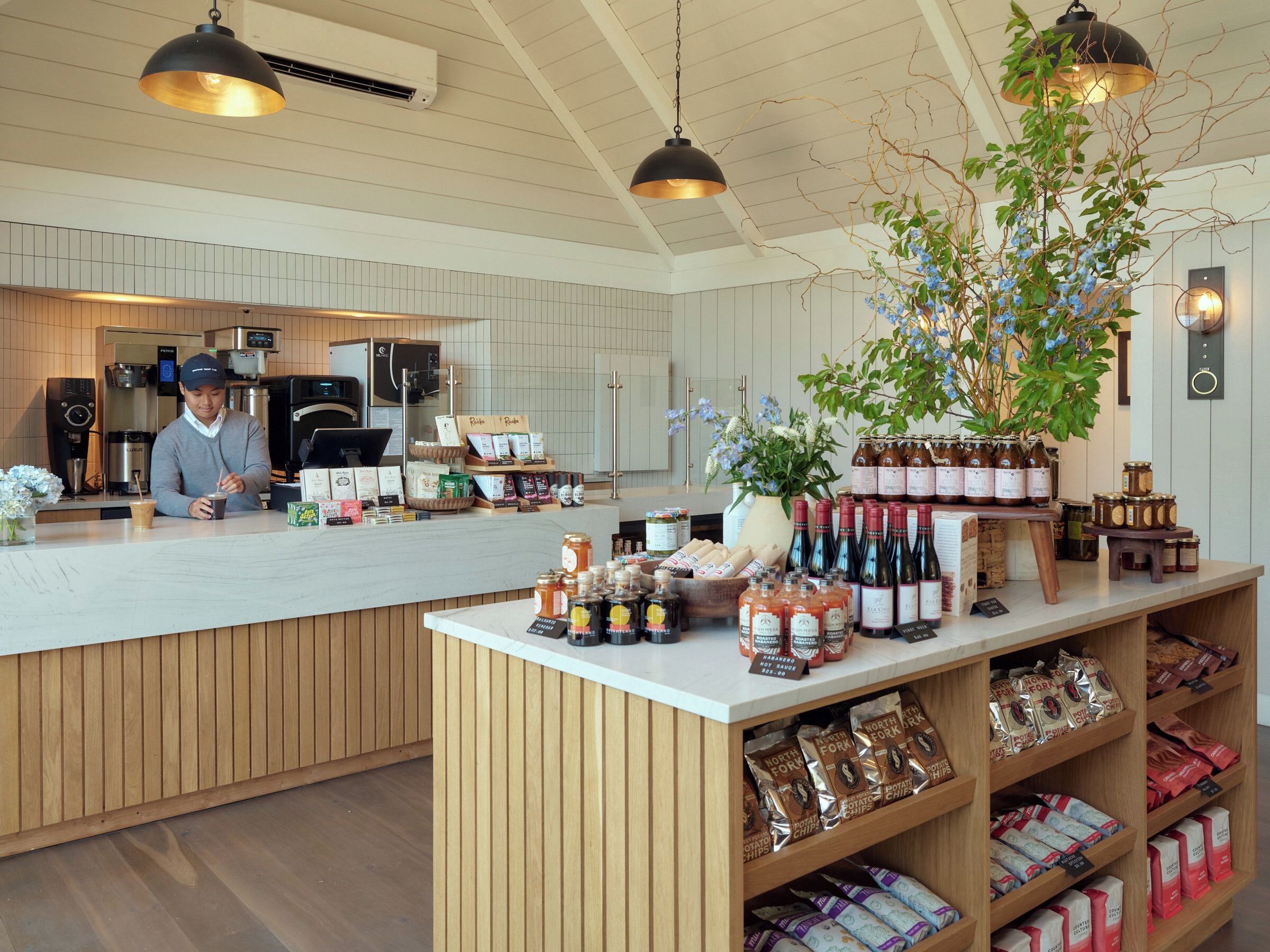 A cafe with a wooden counter, coffee machines, and a variety of food items including chips and jars of condiments.