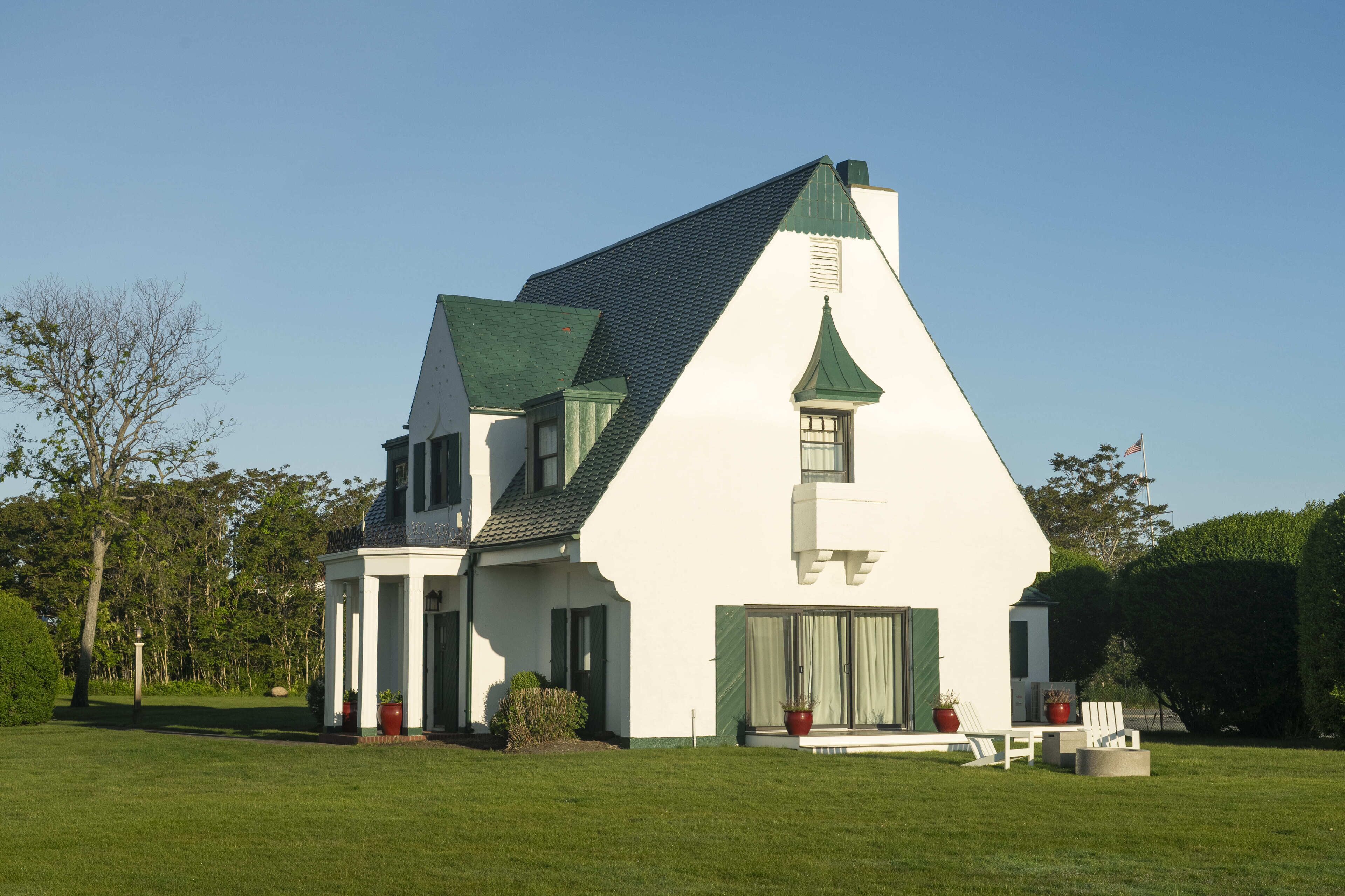 Une maison blanche avec un toit vert et une petite tour, entourée d’une pelouse bien entretenue et d’arbres.