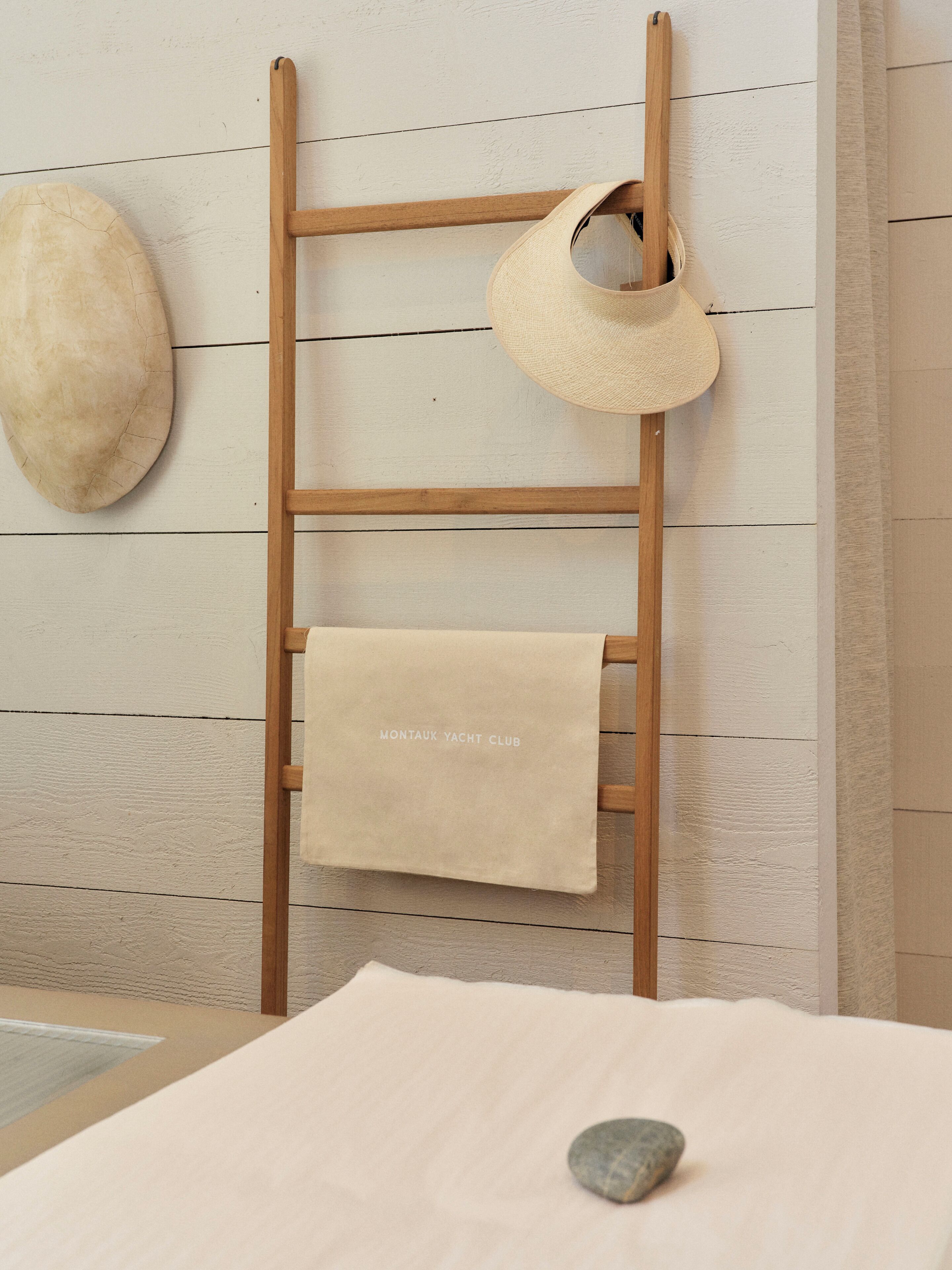 Una escalera de madera con una toalla color crema y un sombrero de paja colgados.