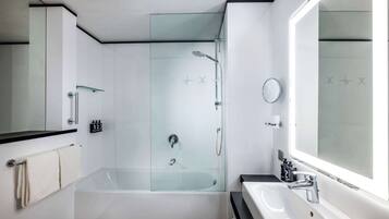 Un baño moderno con ducha de vidrio, una bañera blanca, un lavamanos con espejo y un perchero para toallas.