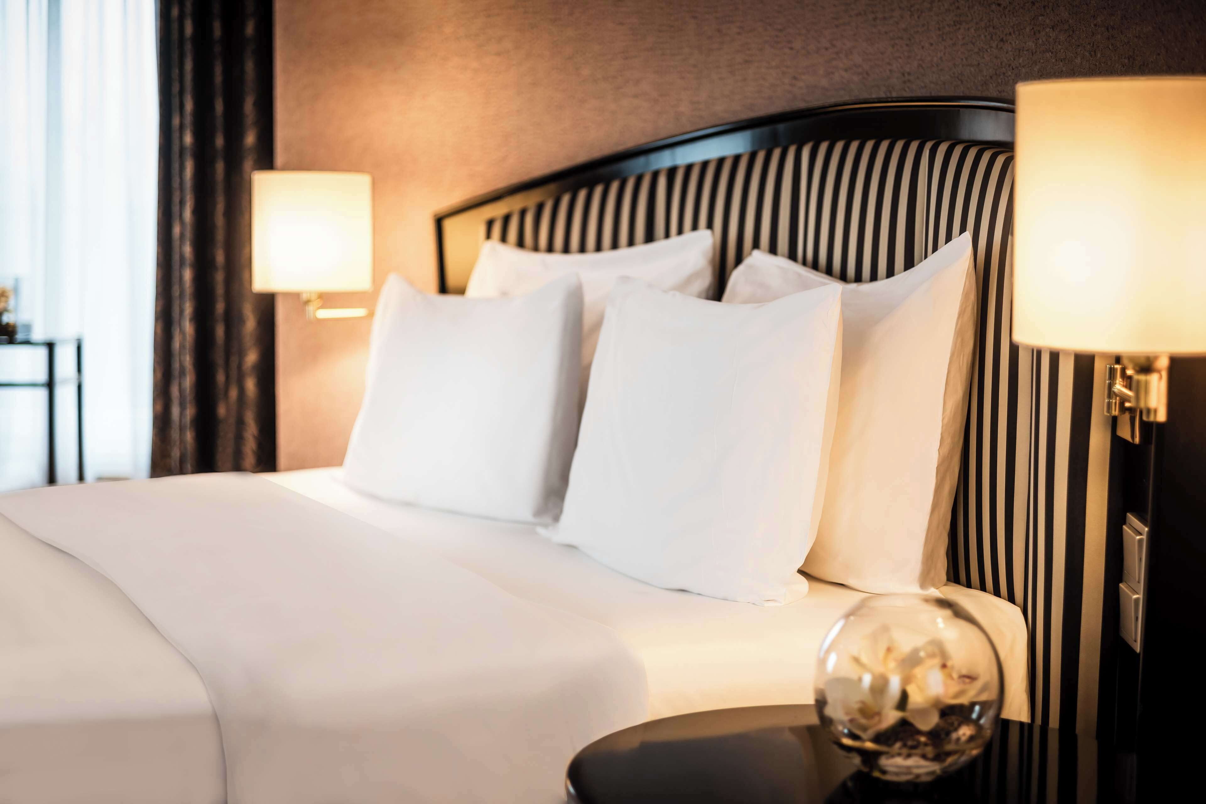A neatly made bed with white linens and pillows, a black-striped headboard, and two bedside lamps.