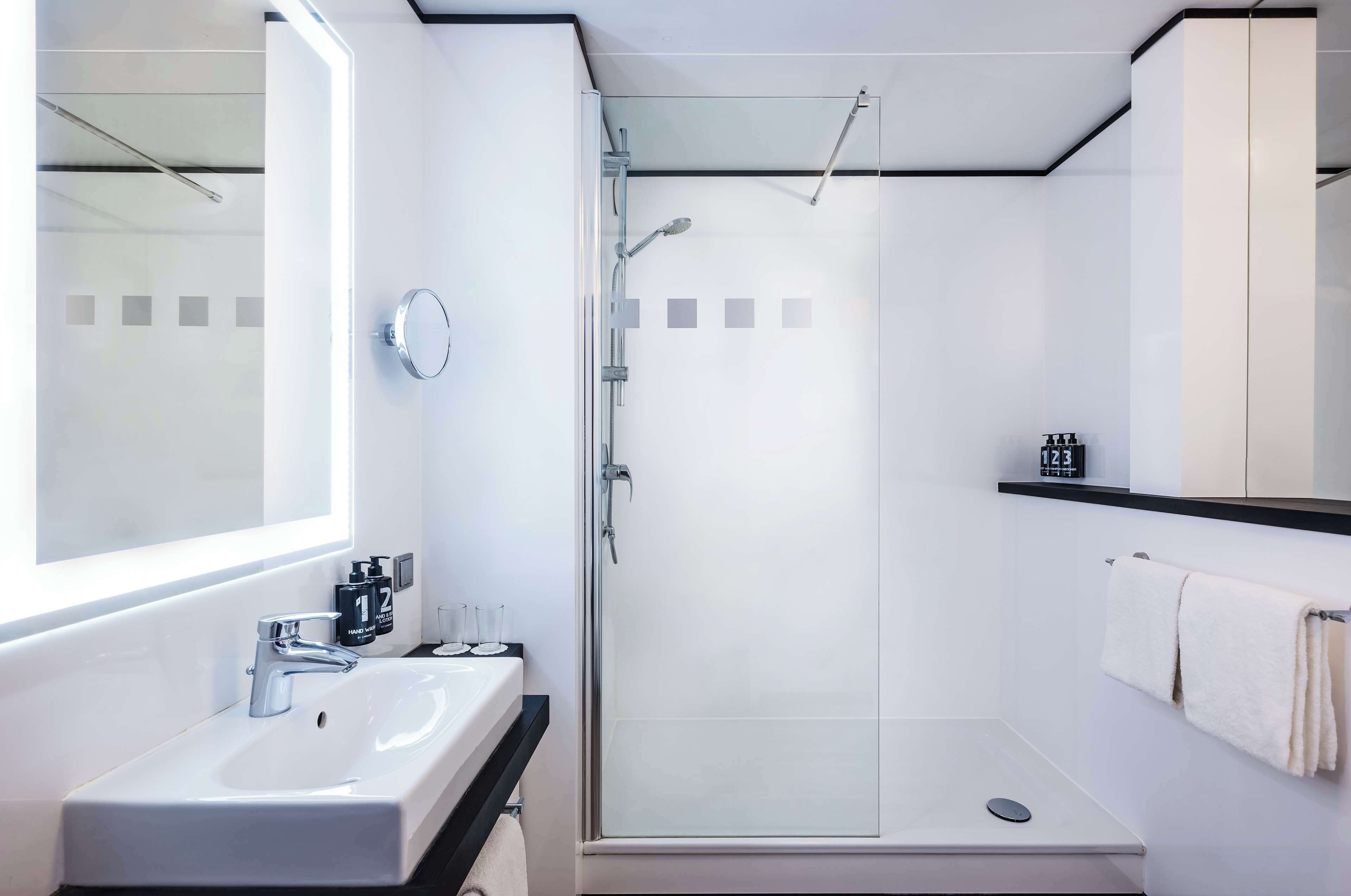 Un baño moderno con un lavamanos blanco, una ducha con mampara de vidrio y un espejo grande.