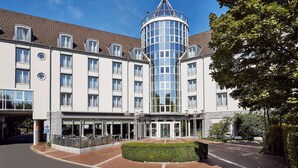 Ein Hotel mit einem zentralen Glasturm, zahlreichen Fenstern und einem gepflegten Eingangsbereich.
