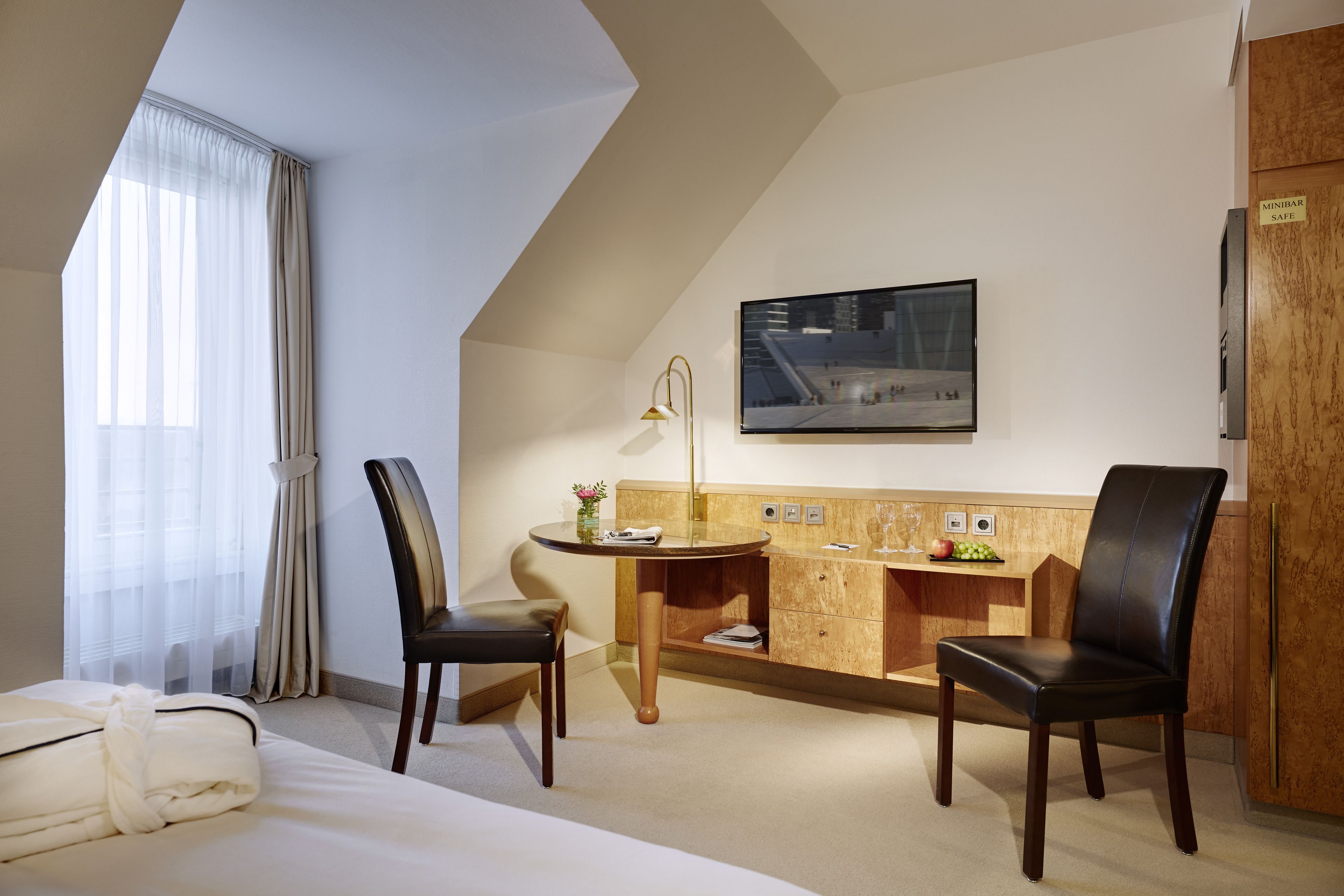 Habitación de hotel con cama, dos sillones, escritorio, lámpara, un cuadro y un minibar.