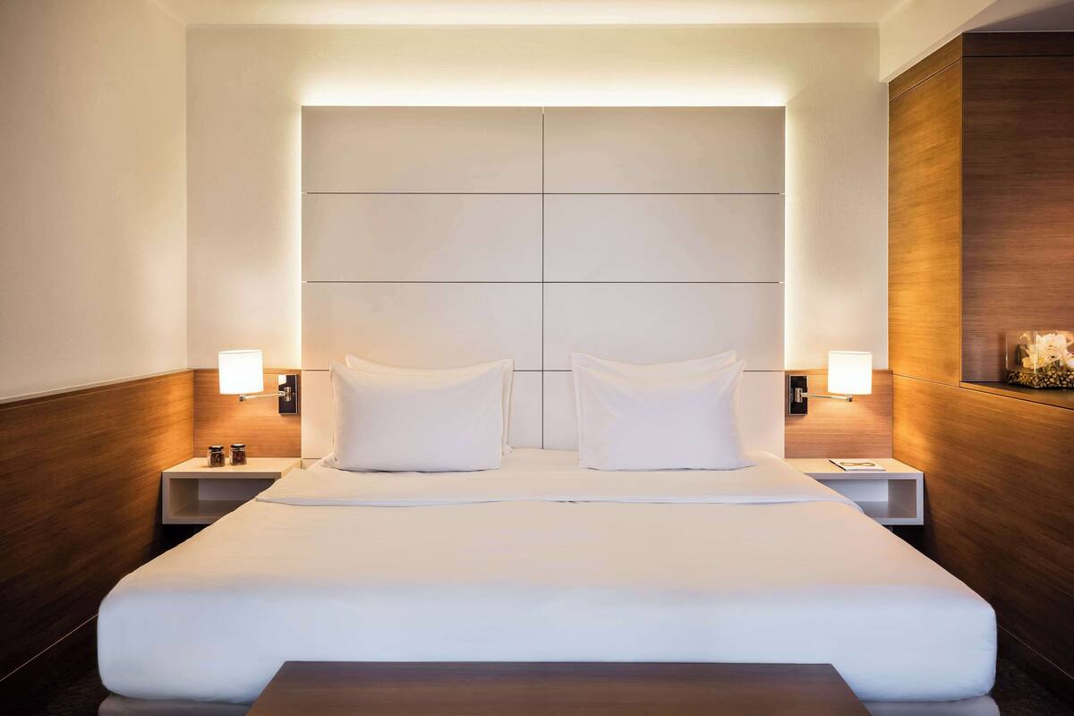 Une chambre d’hôtel moderne avec un grand lit, deux tables de chevet et une tête de lit en bois.