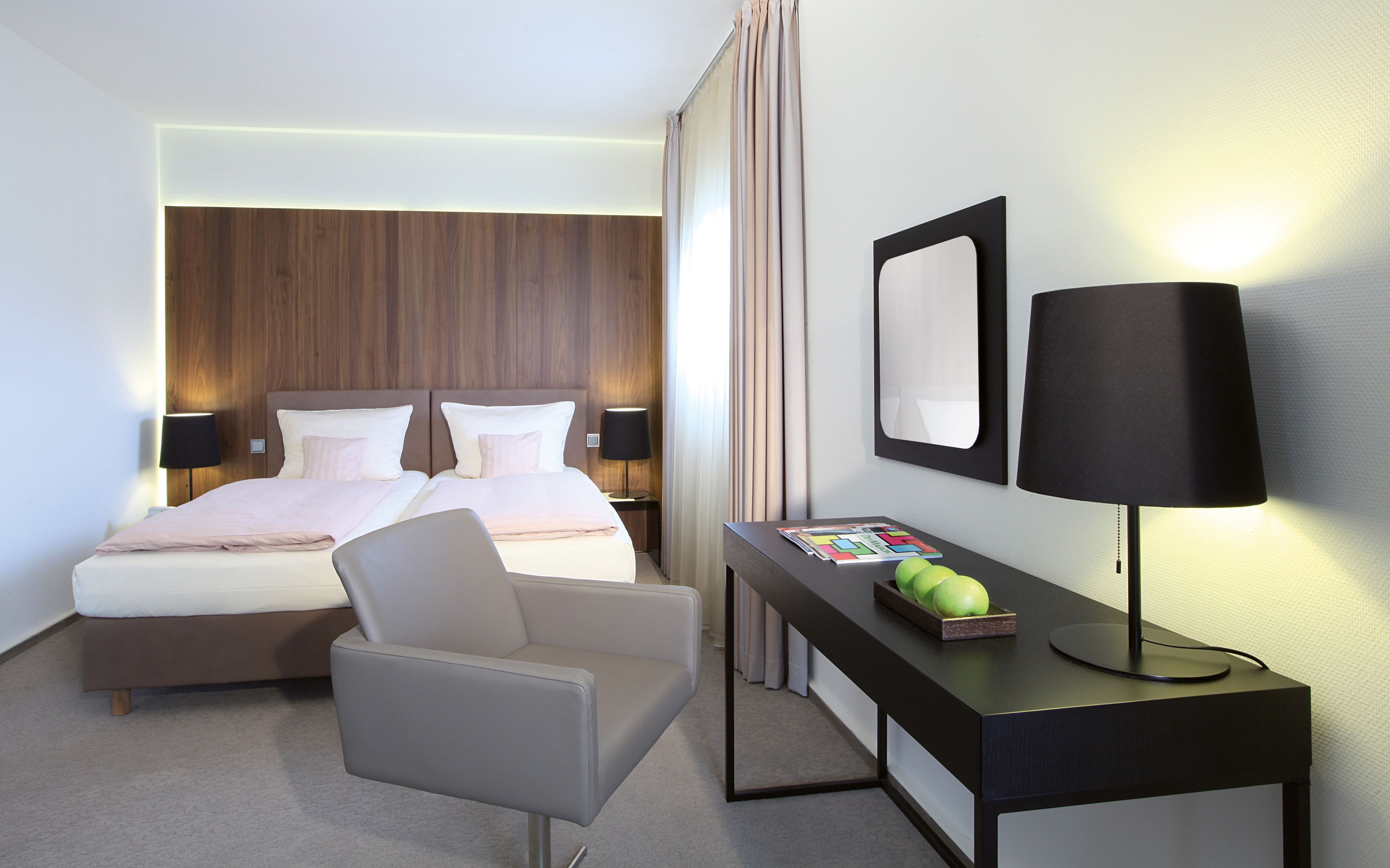Una habitación de hotel con una cama, dos mesitas de noche, un escritorio con una lámpara, una silla y un espejo.