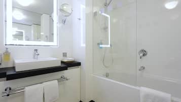 A modern bathroom with a large mirror, a sink, a glass-enclosed shower, and two towels on the floor.