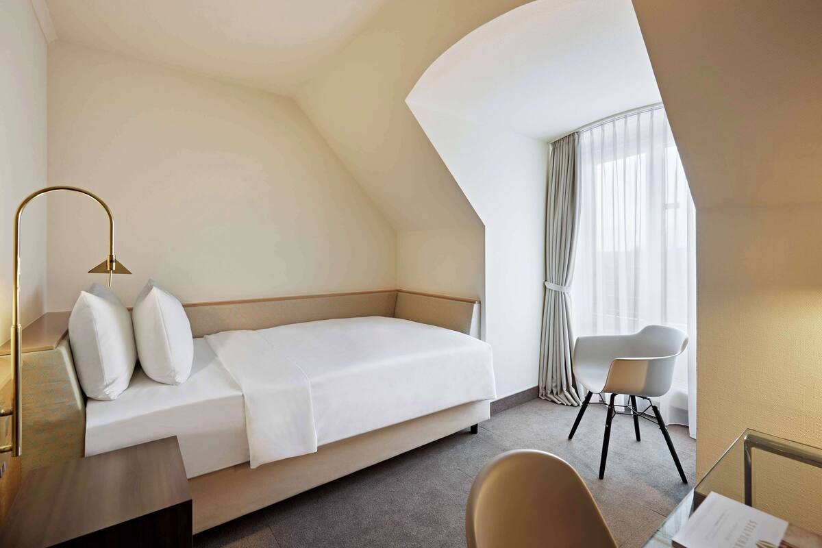 Une chambre d’hôtel moderne équipée d’un lit, d’un bureau, d’une chaise et d’une grande fenêtre avec des rideaux.