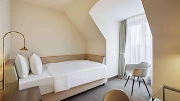 Une chambre d’hôtel moderne équipée d’un lit, d’un bureau, d’une chaise et d’une grande fenêtre avec des rideaux.