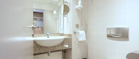 A modern bathroom with a sink, mirror, towel dispenser, and toilet.