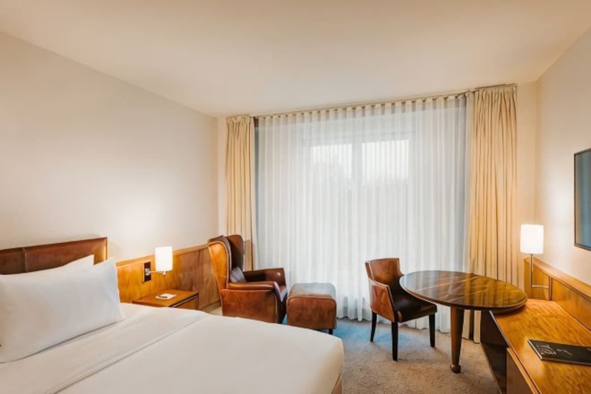 A hotel room with a bed, a desk, a chair, and a window with curtains.