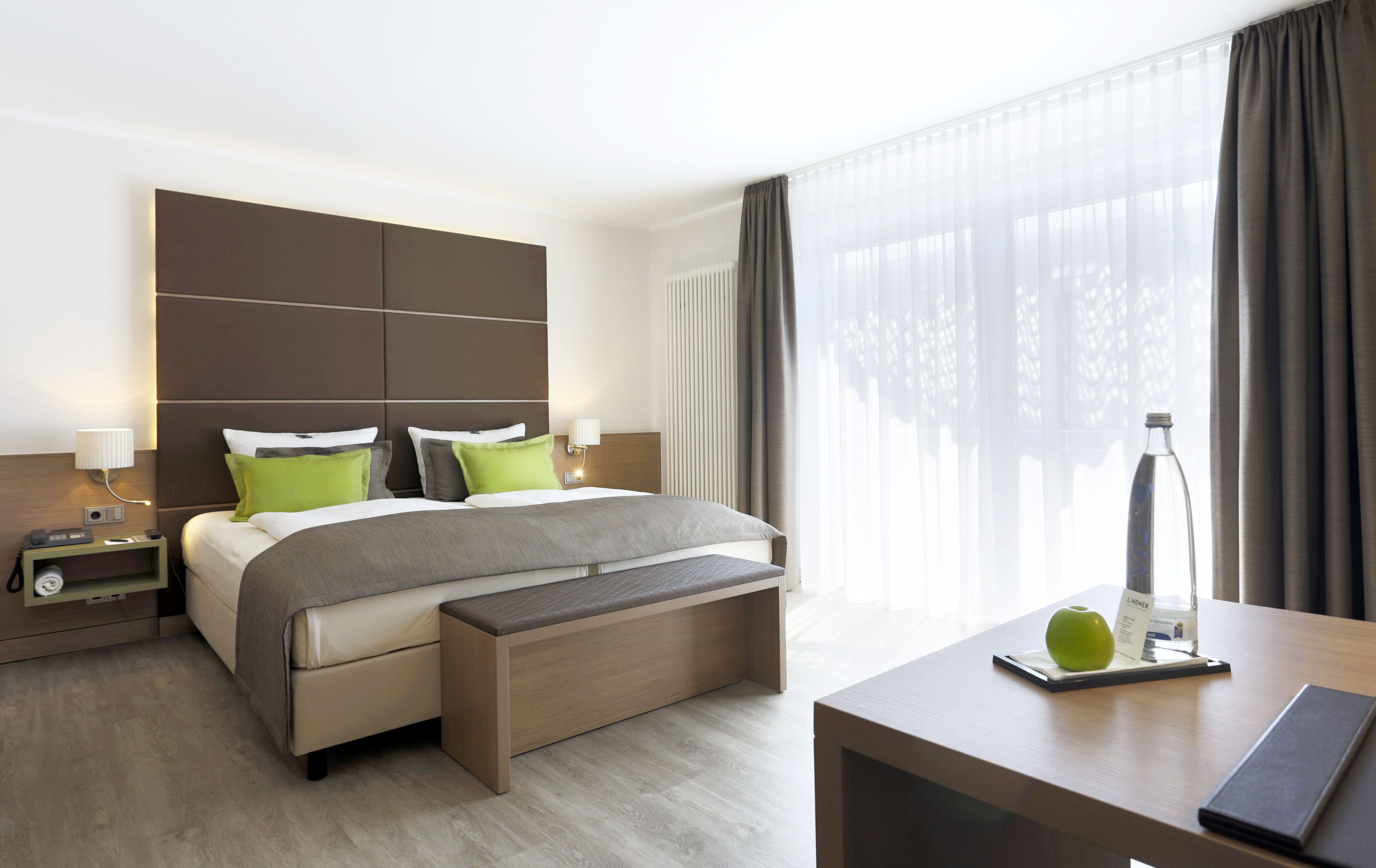 Una habitación de hotel moderna con una cama grande, mesitas de noche, un escritorio y vistas al exterior.