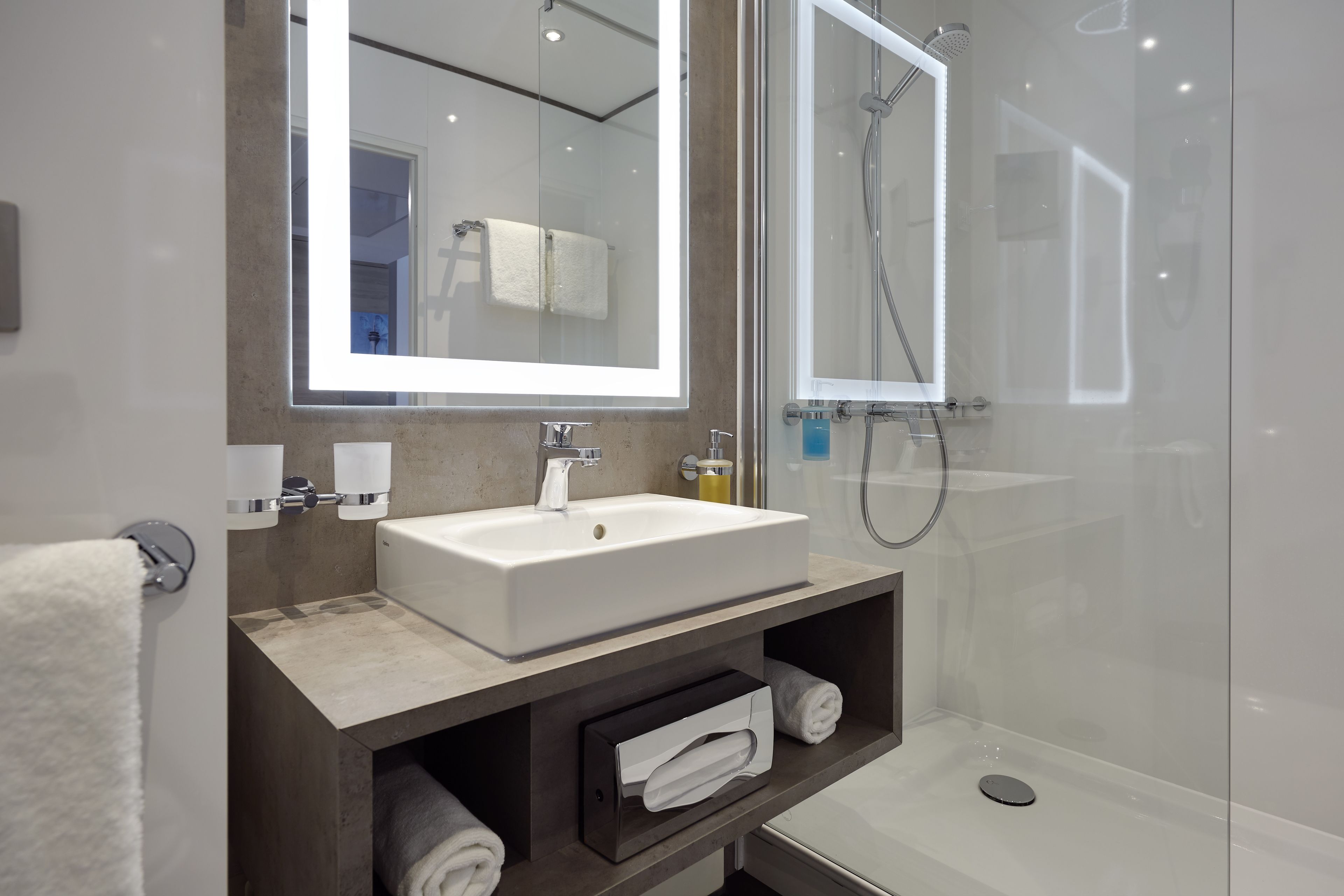 A modern bathroom with a large mirror, a sink, a shower, and a towel rack.