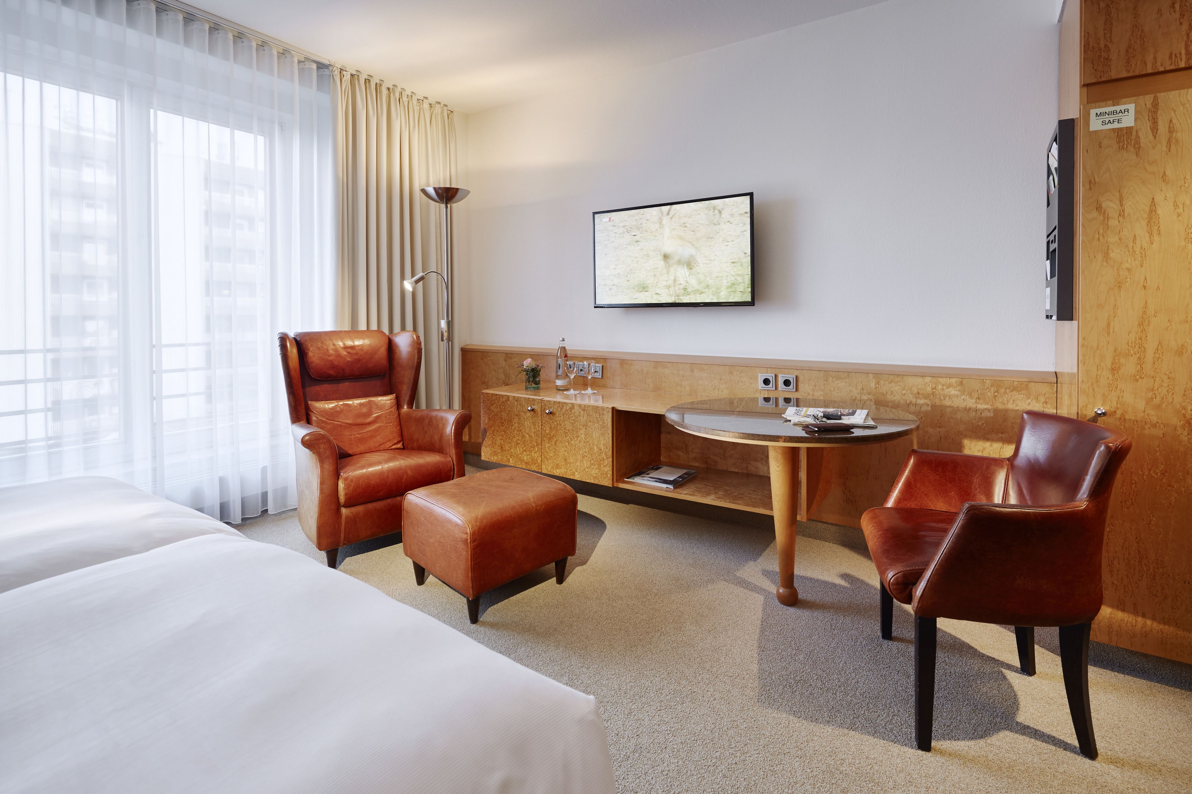 Une chambre d’hôtel avec deux lits, un canapé, une chaise, une petite table et un téléviseur fixé au mur.