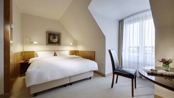 Ein Hotelzimmer mit einem großen Bett, einem Schreibtisch mit Stuhl, einem Fenster mit Vorhängen und einer Wandlampe.