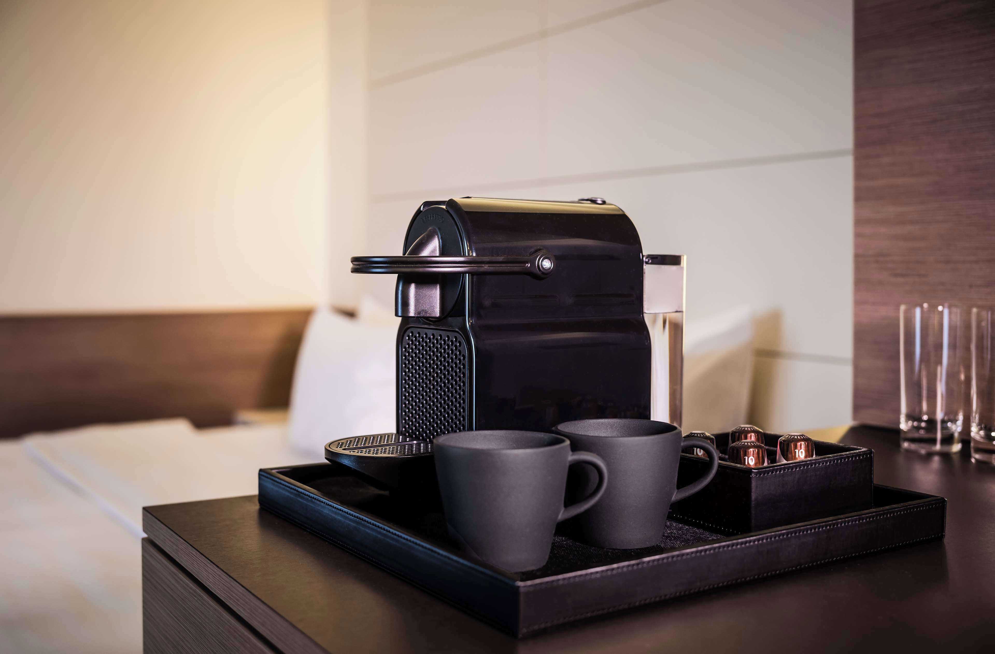 A coffee maker on a tray with two mugs and a small container, likely for coffee grounds, in a hotel room.
