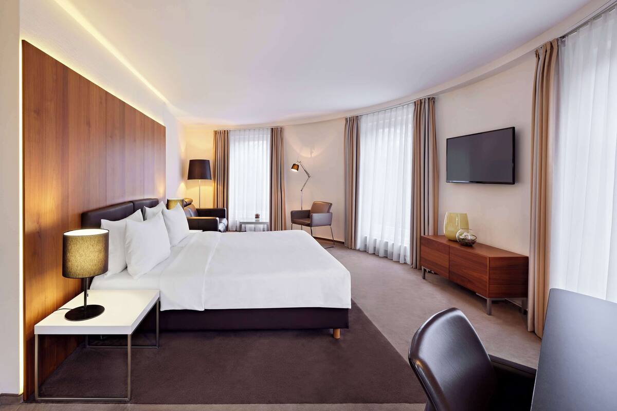 Une chambre d’hôtel avec un grand lit, des tables de chevet, un bureau, une chaise, une télévision et une lampe.