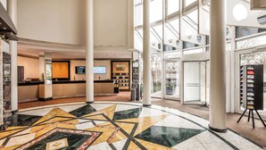 Eine großzügige Lobby mit einem geometrisch gemusterten Boden, einem Empfangstisch und einem großen Fenster mit Blick ins Freie.