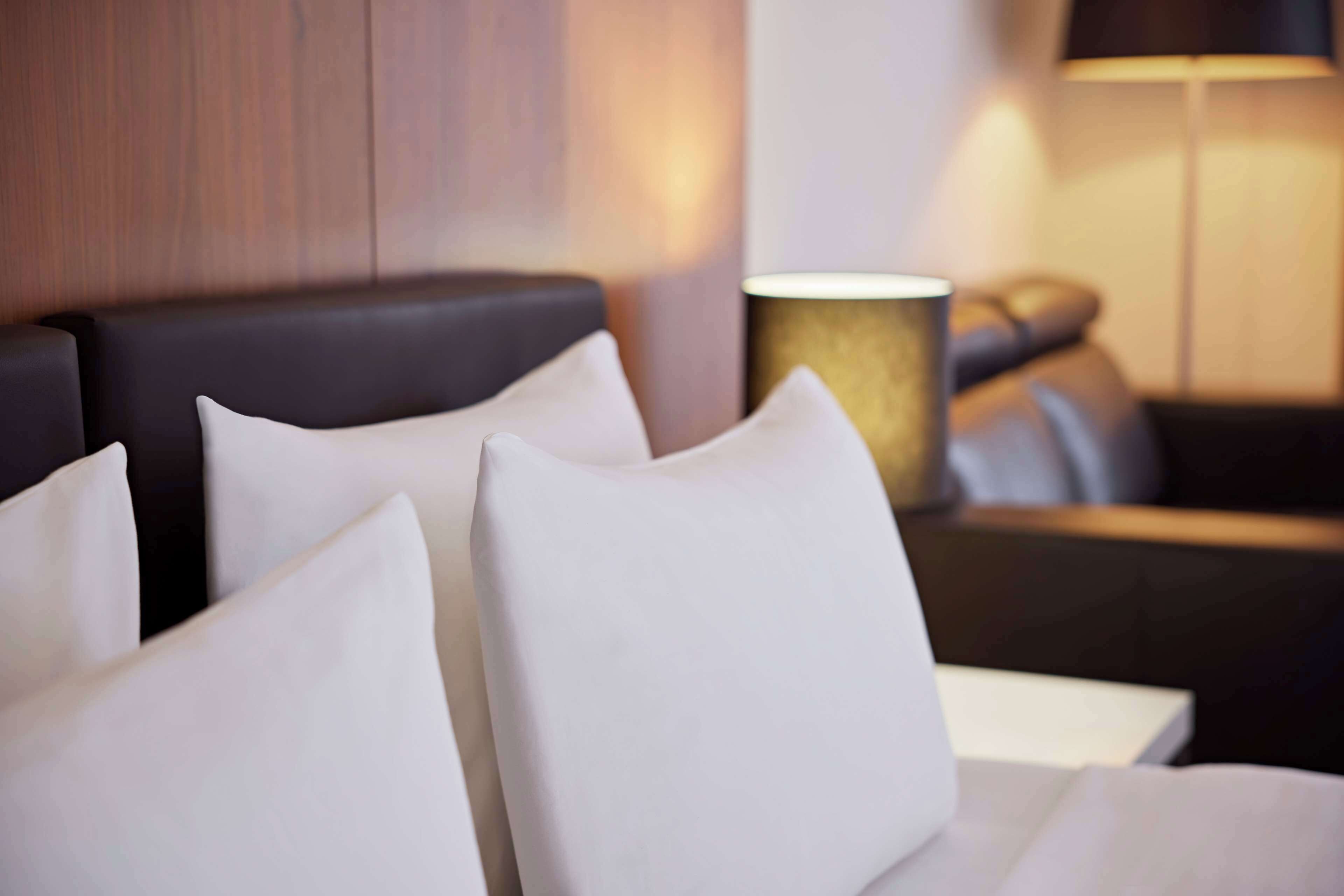 A hotel room with a bed, white pillows, a black headboard, and a lamp.
