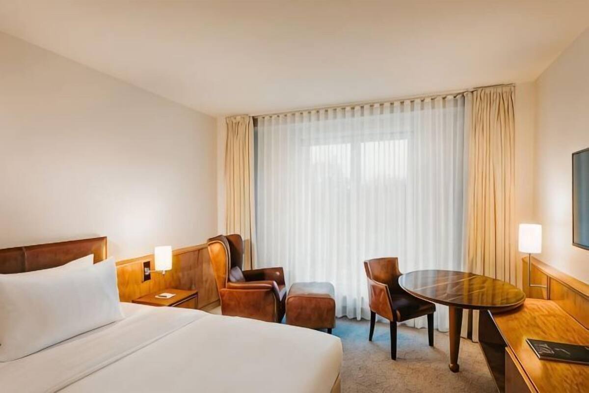 Une chambre d’hôtel avec un lit, un bureau, une chaise, une table et une fenêtre avec des rideaux.