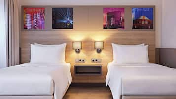 Habitación de hotel con dos camas, cabecero de madera, lámparas de pared y una obra de arte con vistas a la ciudad.