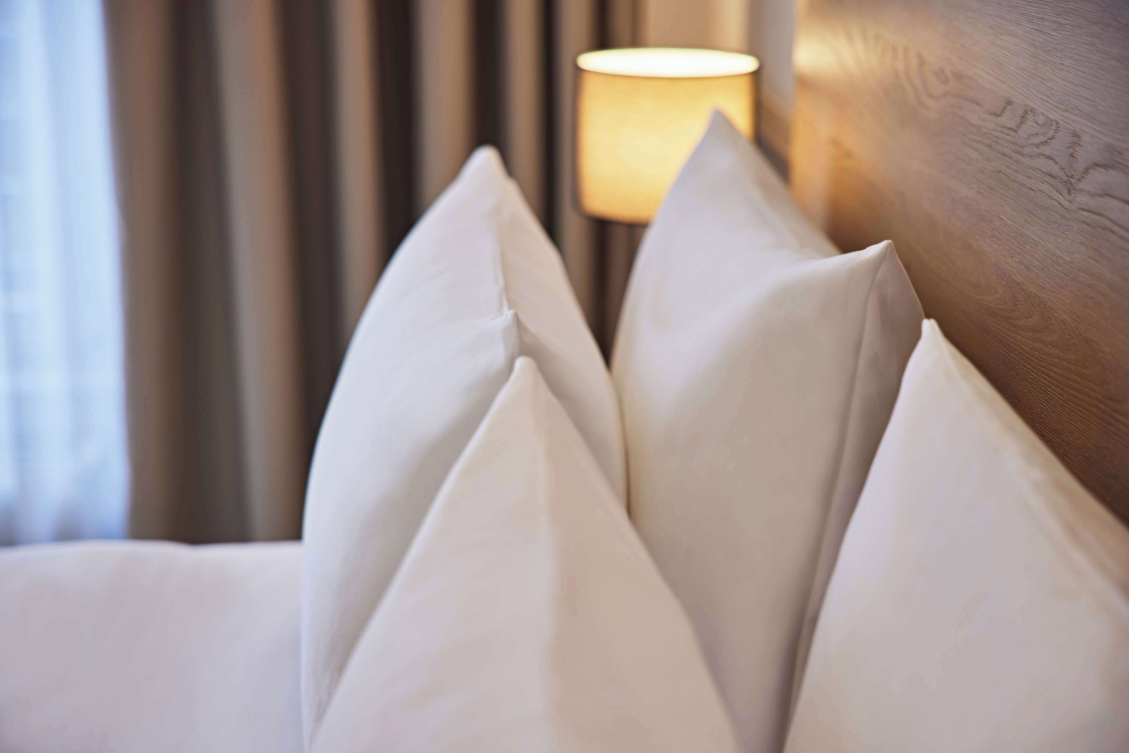 Primer plano de una cama con almohadas blancas y un cabecero de madera.