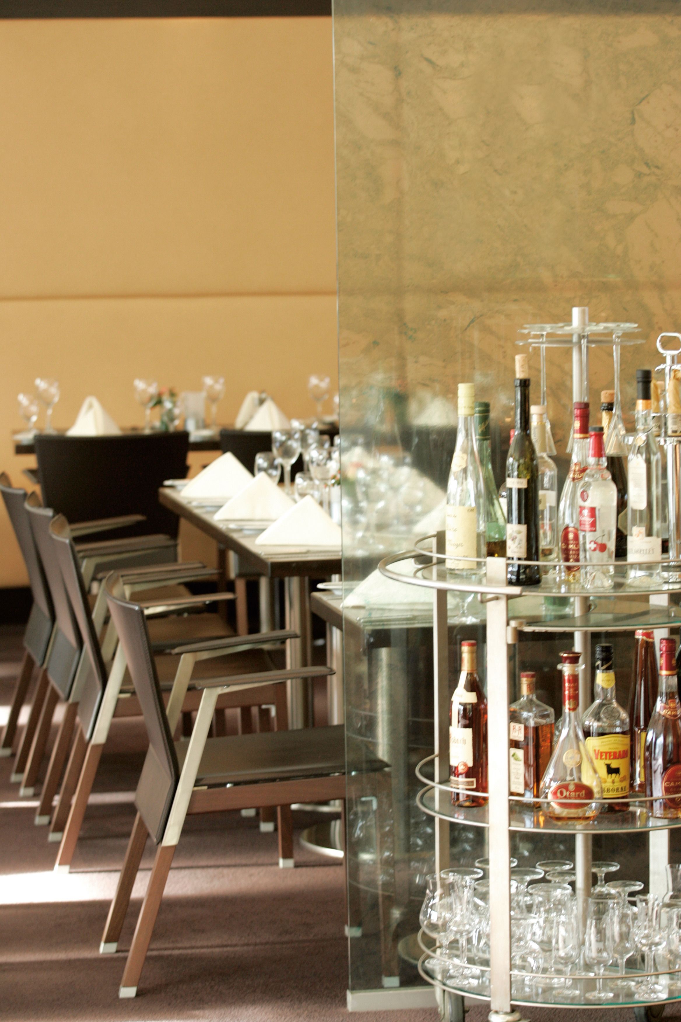 A restaurant with a long table set for dining, chairs, and a bar area with bottles and glasses.