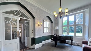 A grand room with a piano, a red sofa, and a chandelier. - Grafton Manor (Bromsgrove)