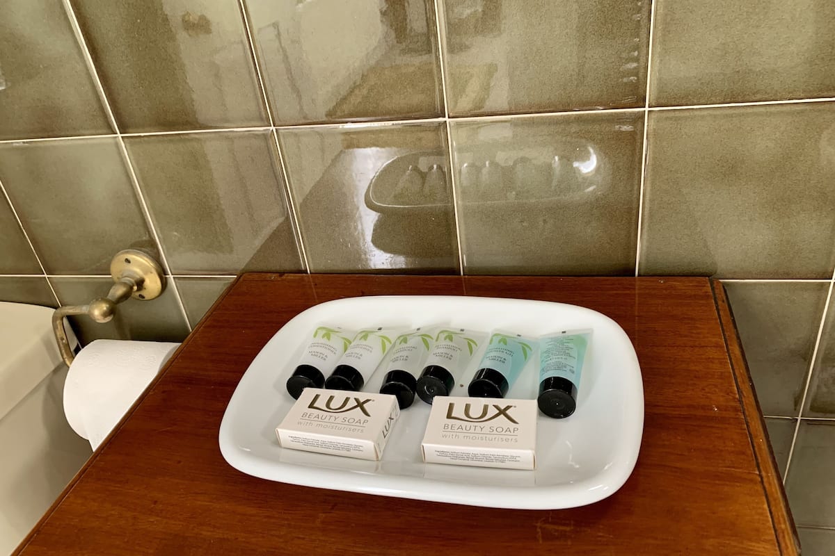 A bathroom with a white sink, a white toilet, and a white tray holding several bottles of Lux Beauty Soap and a box.