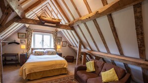 A bedroom with a large bed, a brown sofa, a wooden ceiling, and a hanging ship model. - Grafton Manor (Bromsgrove)
