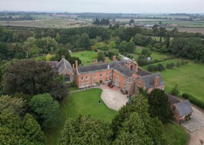 A large, historic building with a symmetrical facade, surrounded by lush greenery and open fields. - Grafton Manor (Bromsgrove)