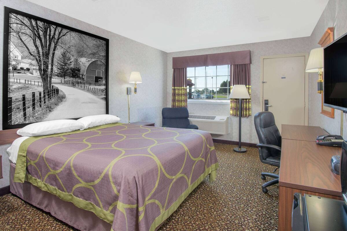 Hotelkamer met een groot bed, een bureau, een stoel, een televisie en een raam met gordijnen.