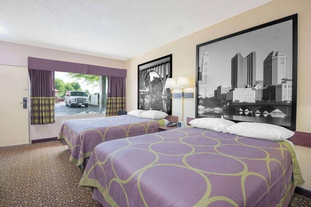 Een hotelkamer met twee bedden, uitzicht op de stad, een raam met gordijnen en een deur naar buiten.