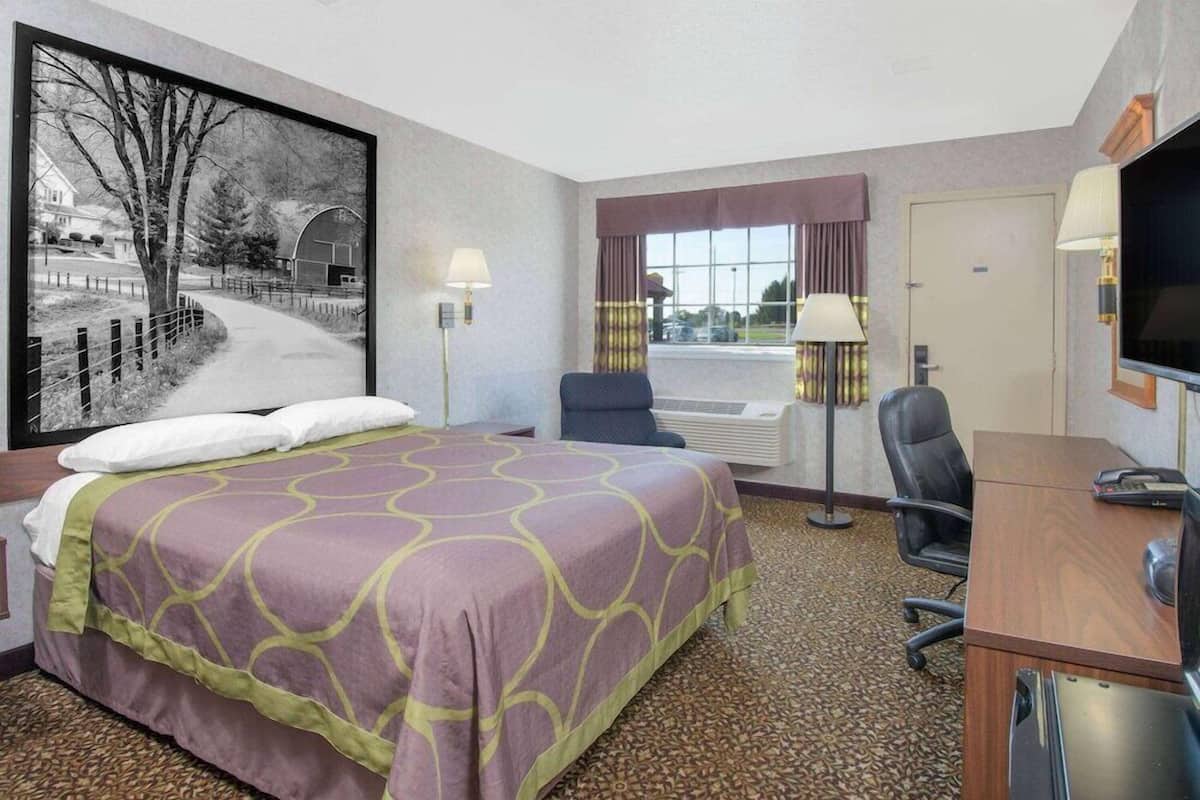 A hotel room with a bed, desk, chair, and a large window.