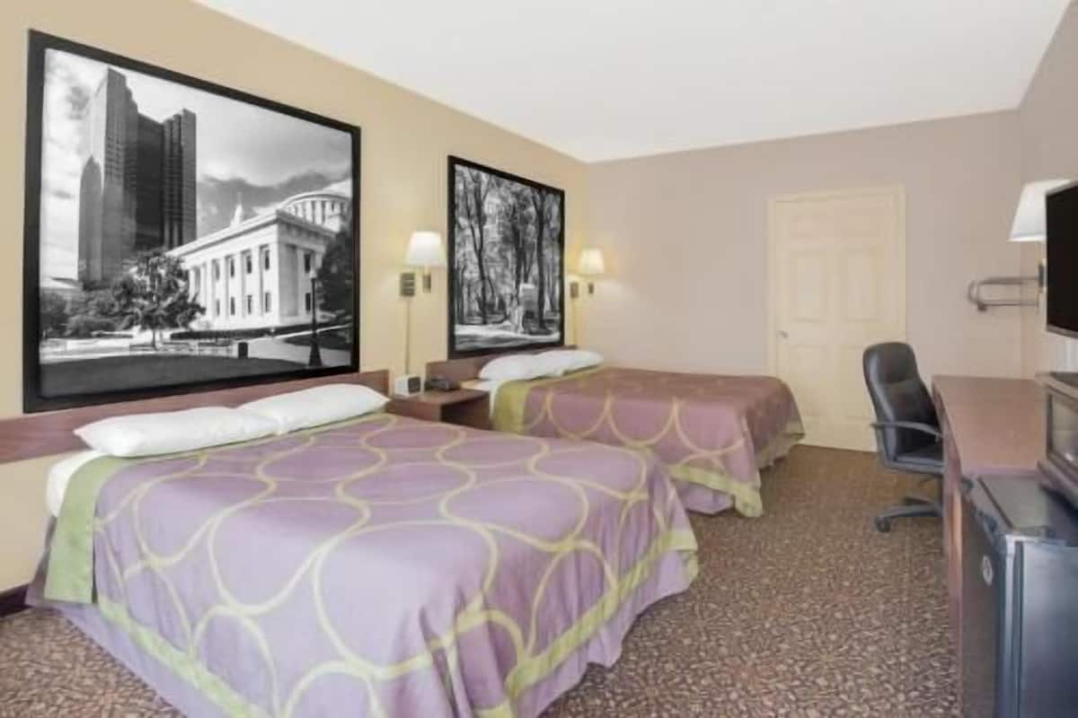 A hotel room with two beds, a desk, a chair, and two framed pictures on the wall.