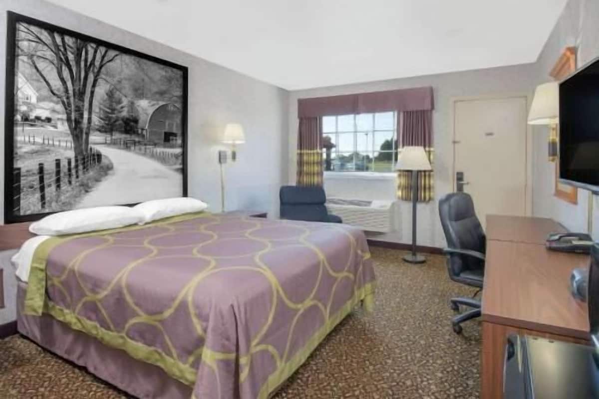 A hotel room with a bed, desk, chair, lamp, and a large window.