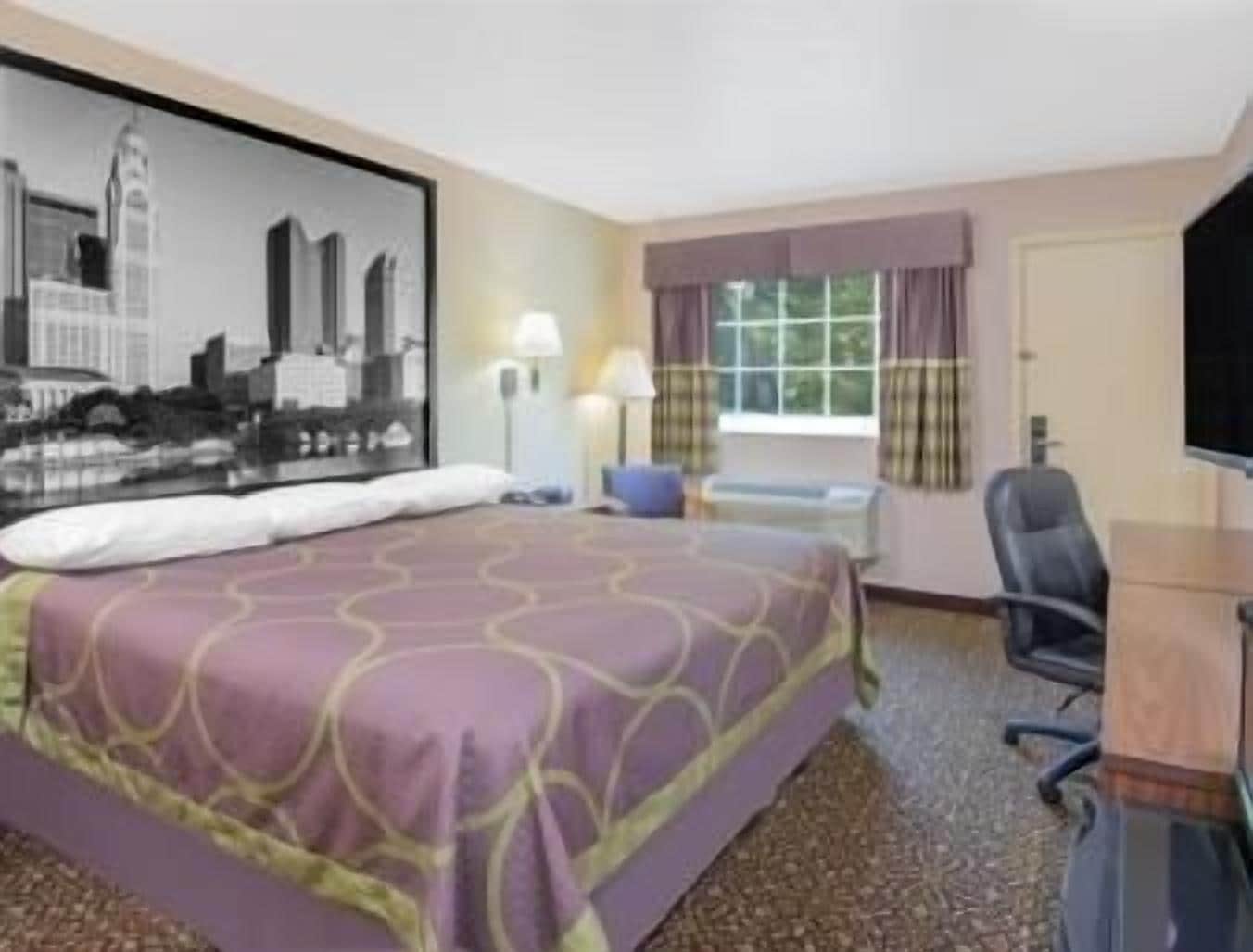Une chambre d’hôtel avec un lit, un bureau, une chaise, une fenêtre avec des rideaux et un tableau représentant un paysage urbain accroché au mur.