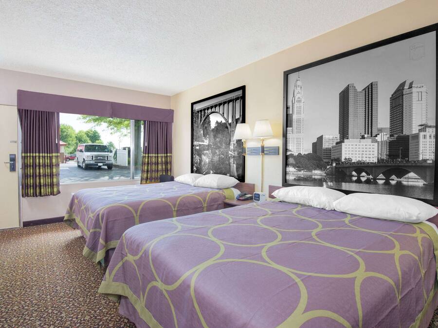 A hotel room with two beds, a cityscape view, a window with curtains, and a lamp.