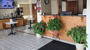 A hotel lobby with a reception desk, a television displaying a news program, a clock, and potted plants. - Ashland Inn & Suites (Ashland)